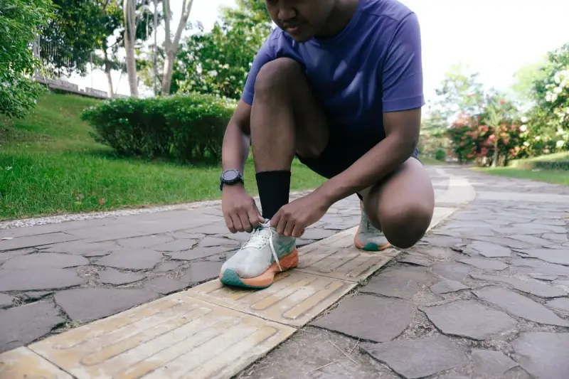Runner in a purple shirt crouching to tie his shoes on a park path