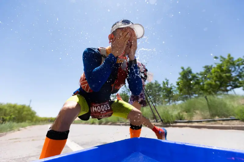 Race runner splashing water on his face at an aid station under a blue sky