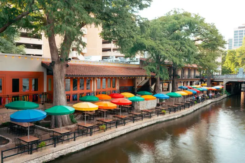 Colorful umbrellas over riverside restaurant tables along the San Antonio River Walk