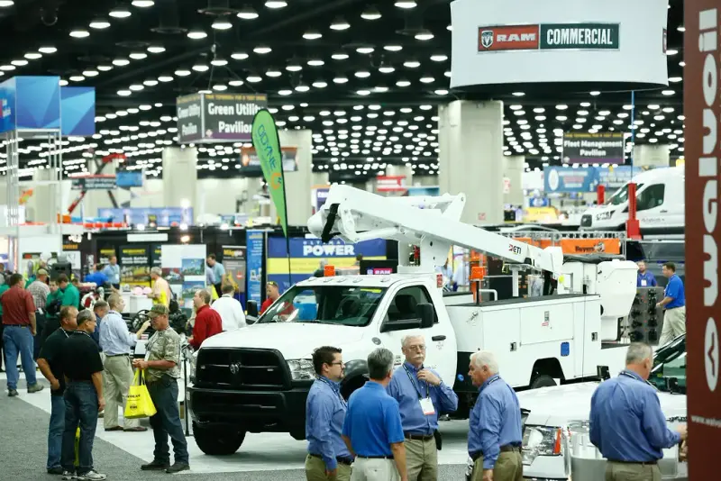 Attendees walking an indoor hall lined with service trucks and pavilion signs