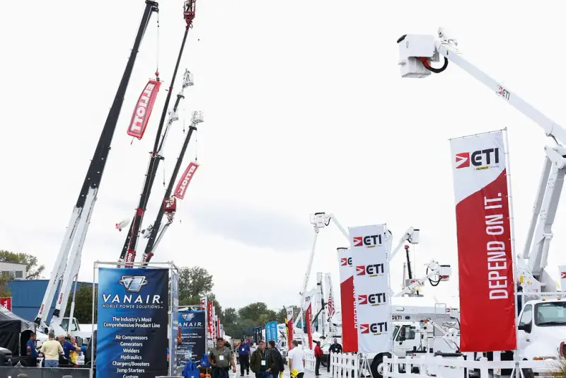 Raised aerial lifts and cranes above banners in an outdoor exhibit lot