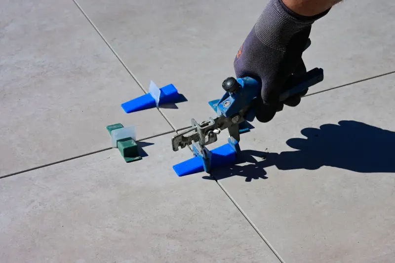 Gloved hand tightening a tile leveling clip between large-format tiles