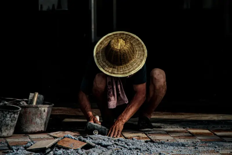 Tile setter in a wicker hat laying terracotta tile in fresh mortar