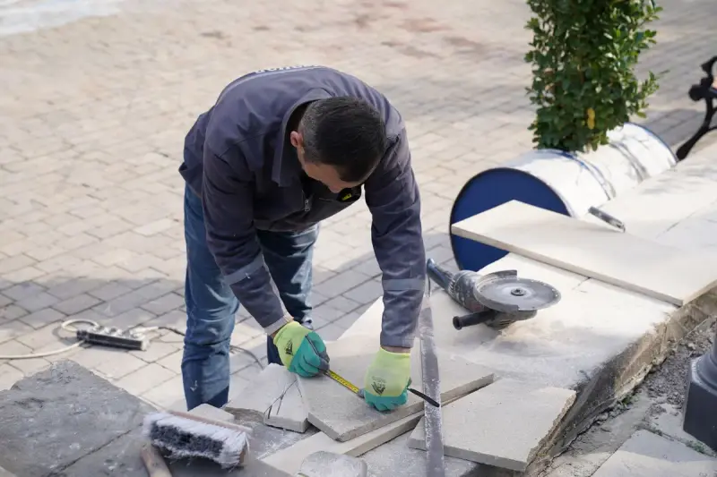 Tile setter measuring stone tiles outdoors with a tape measure