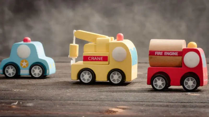 Three small wooden toy vehicles, a police car, crane truck and fire engine, on a wooden table
