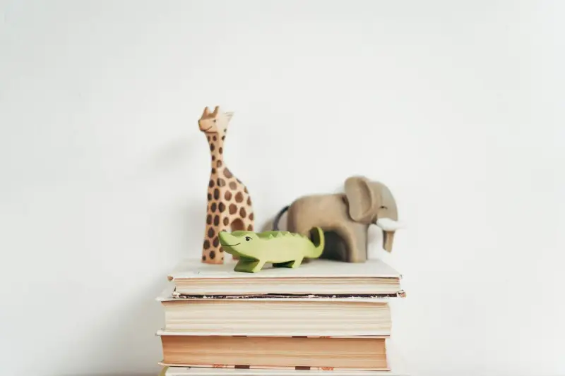 Wooden giraffe, elephant and crocodile toys standing on a stack of books