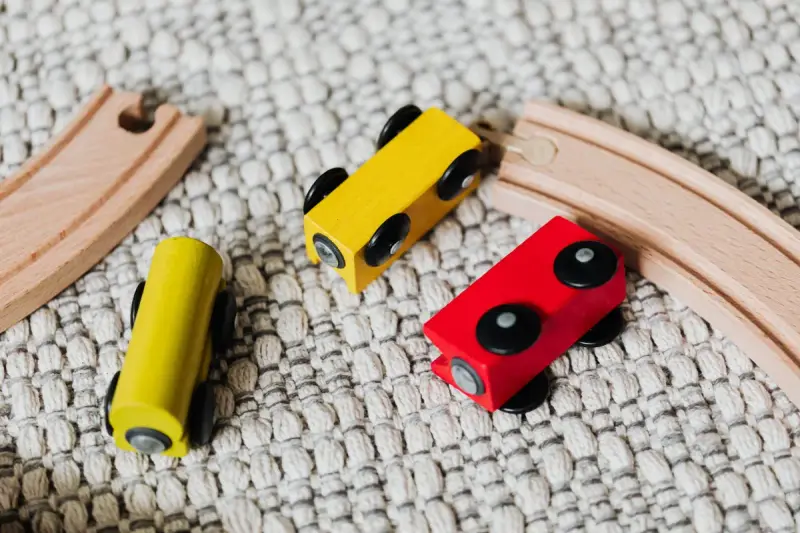 Yellow and red wooden train cars on curved wooden track over a textured rug