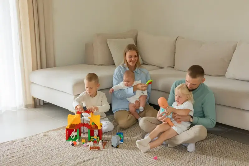 Parents and three young children playing with a toy farm set on a living room rug