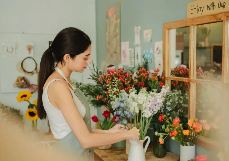 Florist arranging a bouquet of fresh flowers at a wooden counter in her shop