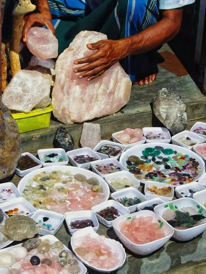 Dealer handling large rose quartz rough above bowls of polished gemstones at a market