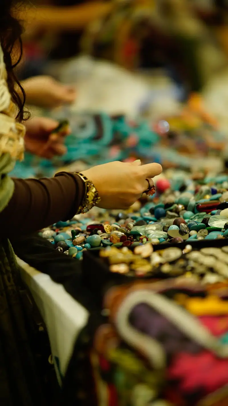 Buyer reaching into a table of colorful gemstones and beads at a gem market