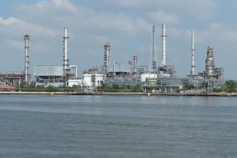 Large oil refinery complex with tall stacks on a waterfront under cloudy skies
