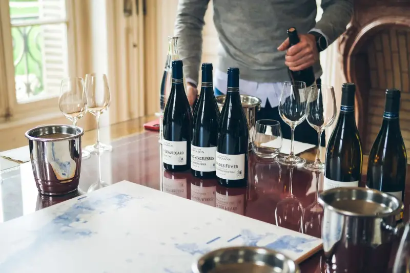 Man opening a wine bottle at a tasting table with glasses, ice buckets and a map
