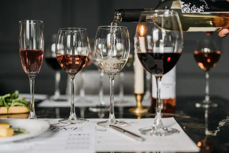 White wine poured into a glass beside rosé and red wines on a tasting sheet