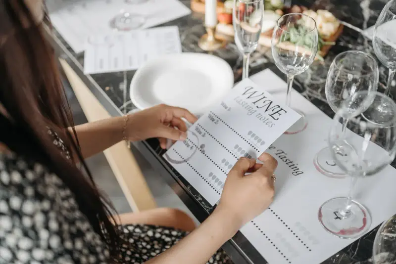 Woman holding a wine tasting notes card at a table set with empty glasses