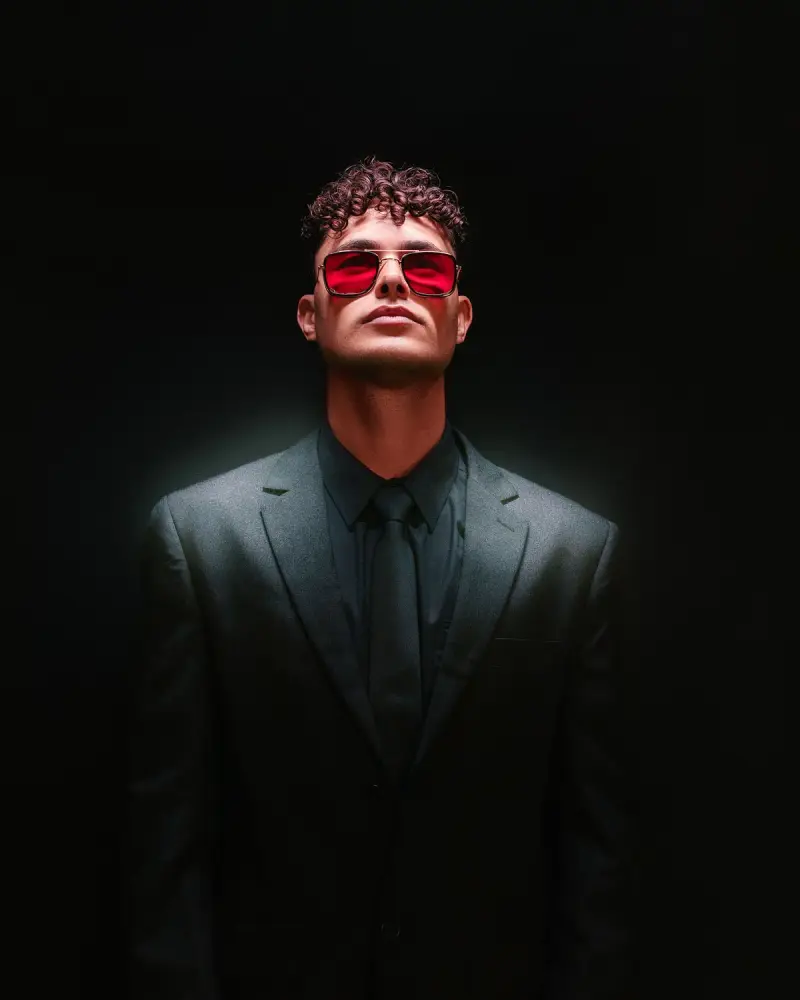 Man in a dark suit and red-lens metal sunglasses, dramatic studio light