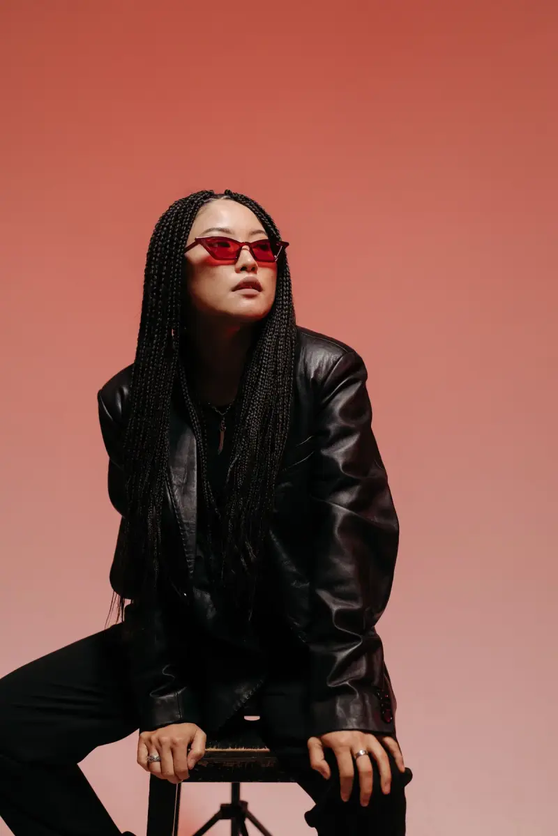 Woman in red cat-eye sunglasses and a leather jacket on a coral studio backdrop