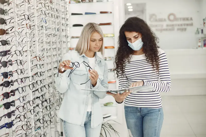 Two women comparing eyeglass frames at an optician's shop