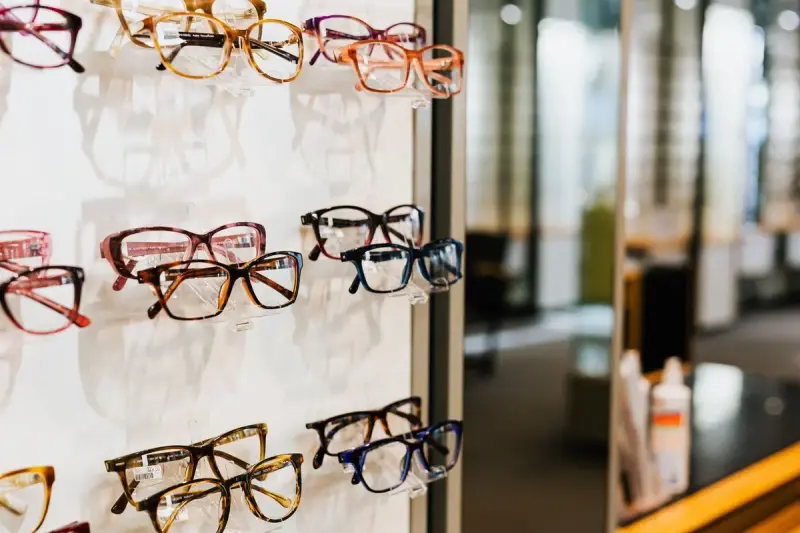 Eyeglass frames in many colors on a white display wall in an optician store