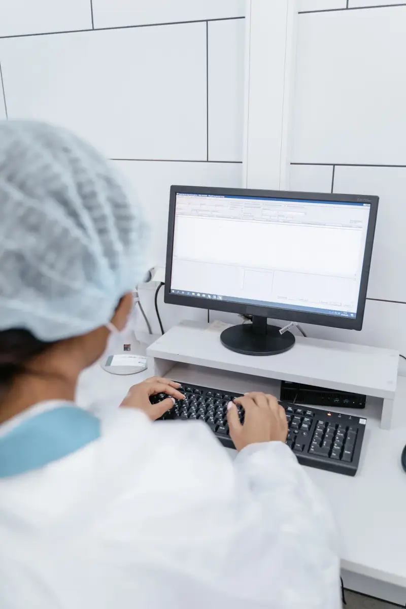 Health worker in a hair cover types into a data entry screen on a desktop computer