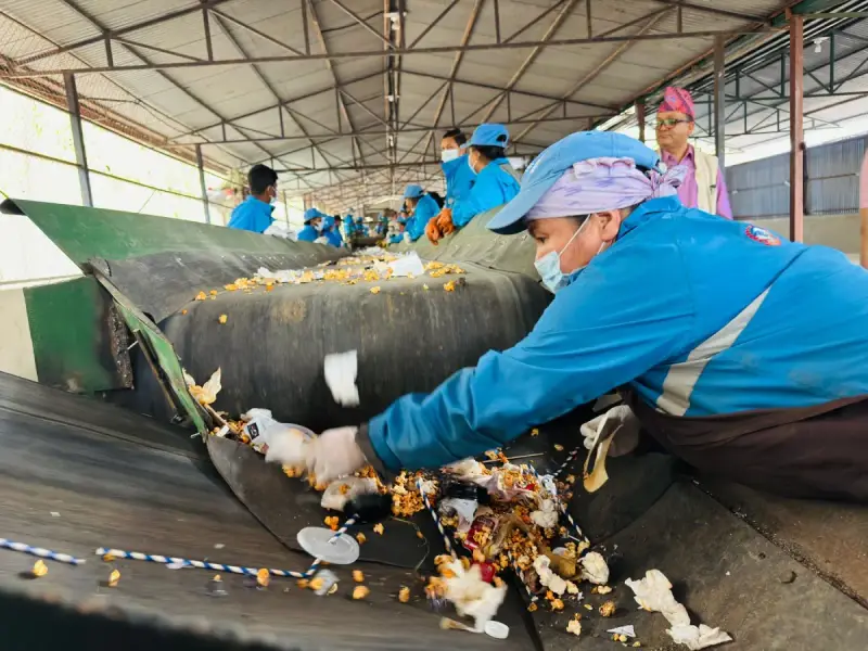 Workers in blue uniforms sorting material on a recycling conveyor in Nepal