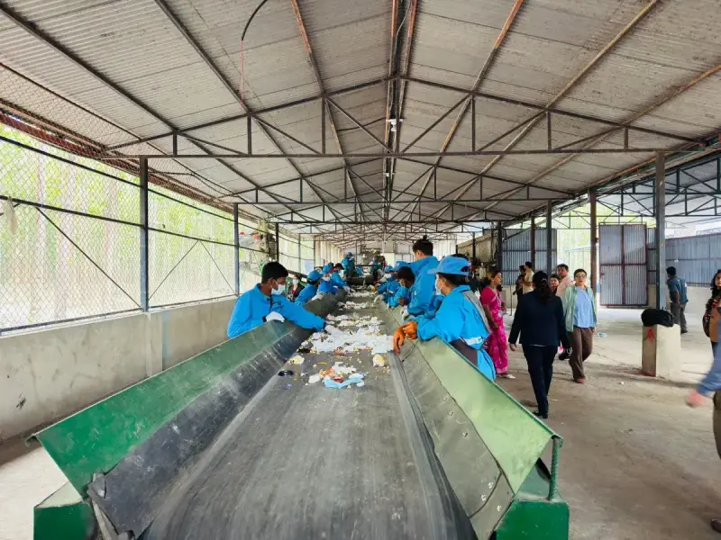 Workers in blue uniforms sorting material at an indoor recycling facility in Butwal