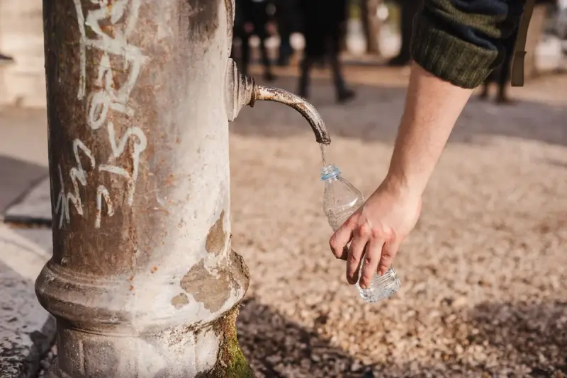 Hand filling a plastic bottle from an old street water fountain