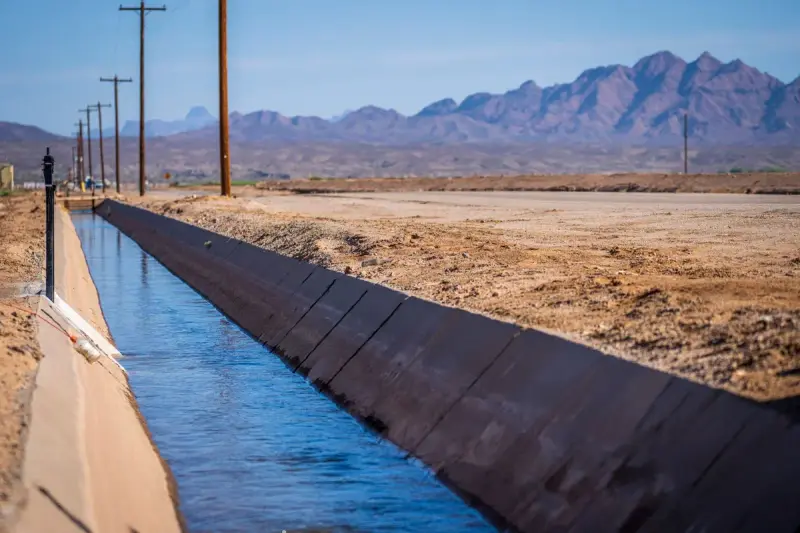 Concrete-lined irrigation canal running through desert toward rugged mountains