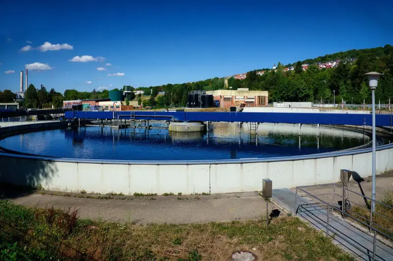 Round clarifier filled with blue water at a sewage treatment plant under a clear sky