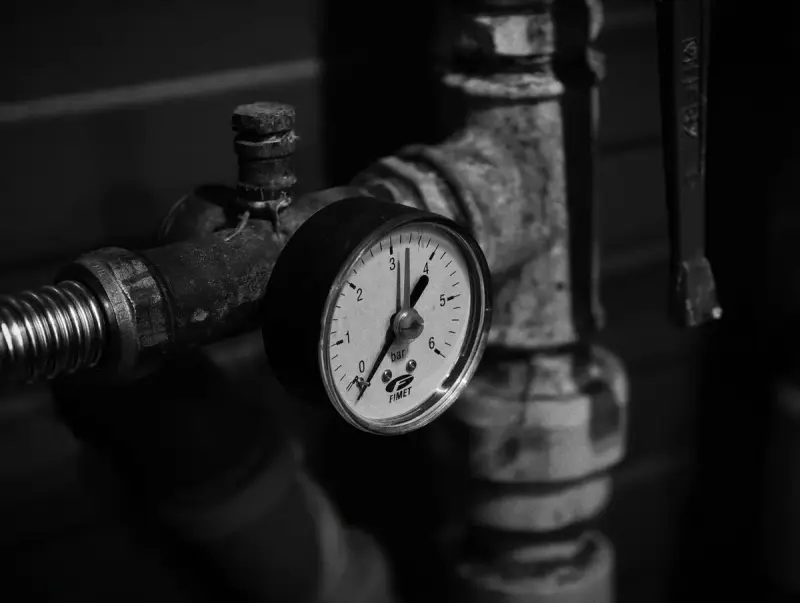 Black and white close-up of a pressure gauge on threaded industrial pipework