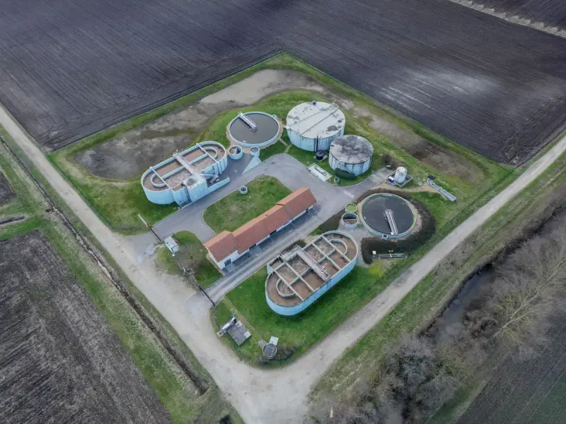 Small rural sewage treatment plant with round tanks seen from above between fields