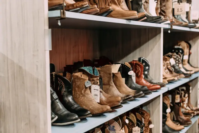 Rows of cowboy boots in black, brown and tooled leather on store shelves with size tags