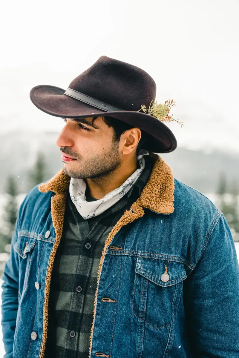 Bearded man in a felt cowboy hat and sherpa-lined denim jacket over a plaid shirt