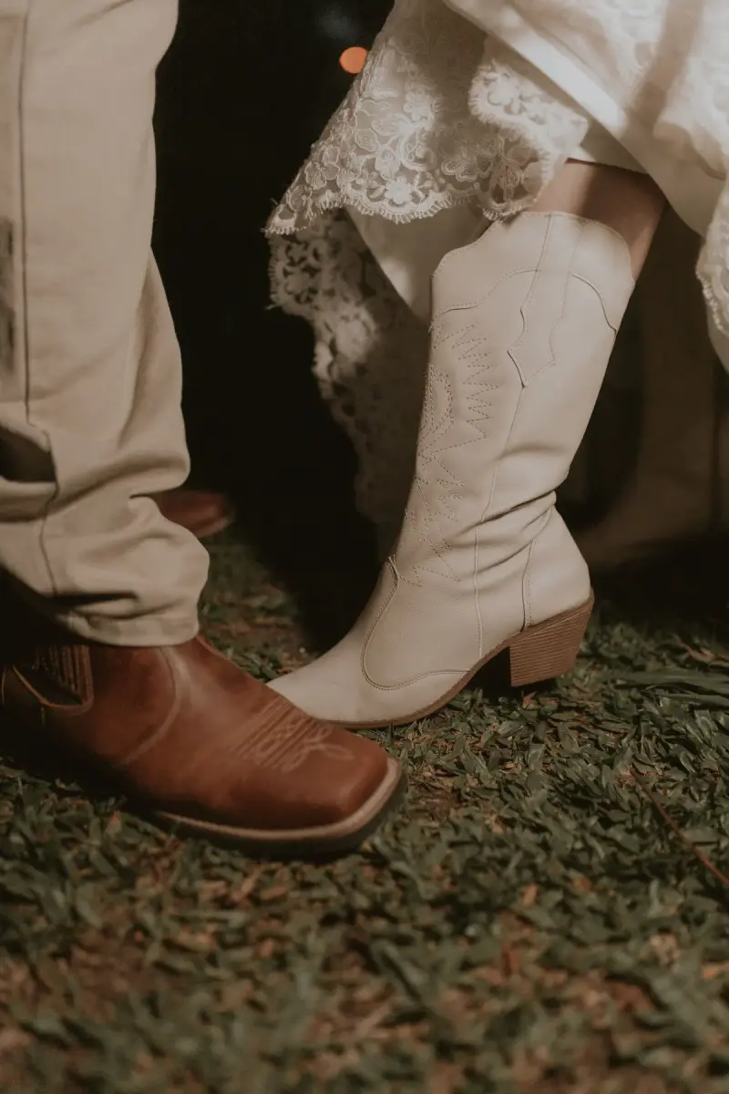 Close-up of a couple's cowboy boots, brown leather and white stitched, dancing on grass