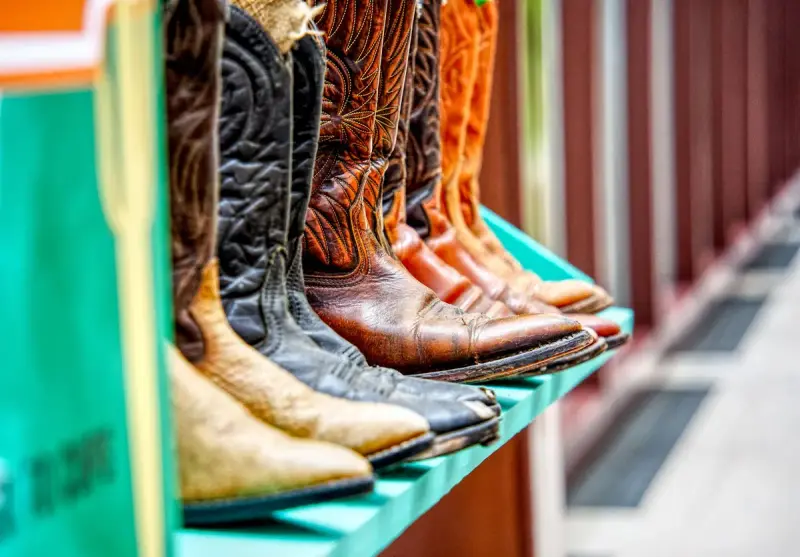 Embroidered leather cowboy boots in black, brown and orange standing on a turquoise shelf