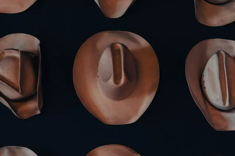 Overhead view of felt cowboy hats in warm brown tones on a dark background