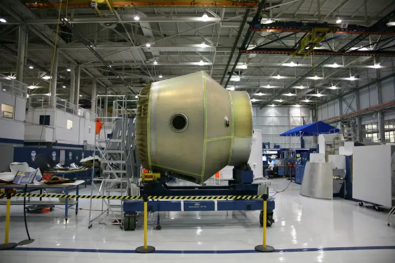 Spacecraft section on a cradle in a bright, clean aerospace assembly hall