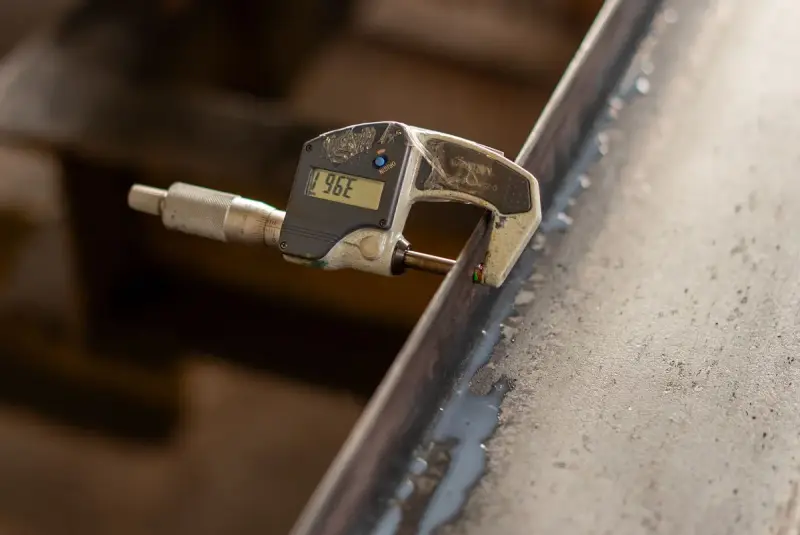 Digital micrometer clamped on the edge of a steel part, reading in fine units