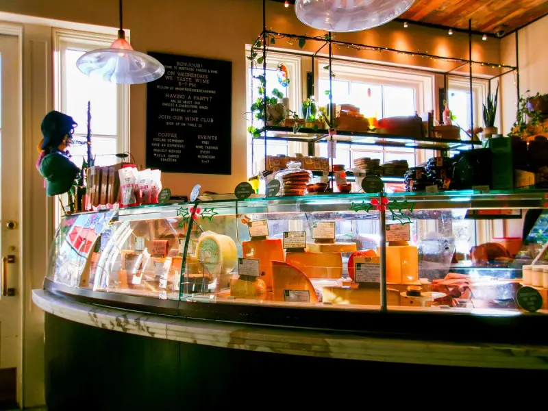 Curved glass cheese case with labeled wedges and wheels in a gourmet shop