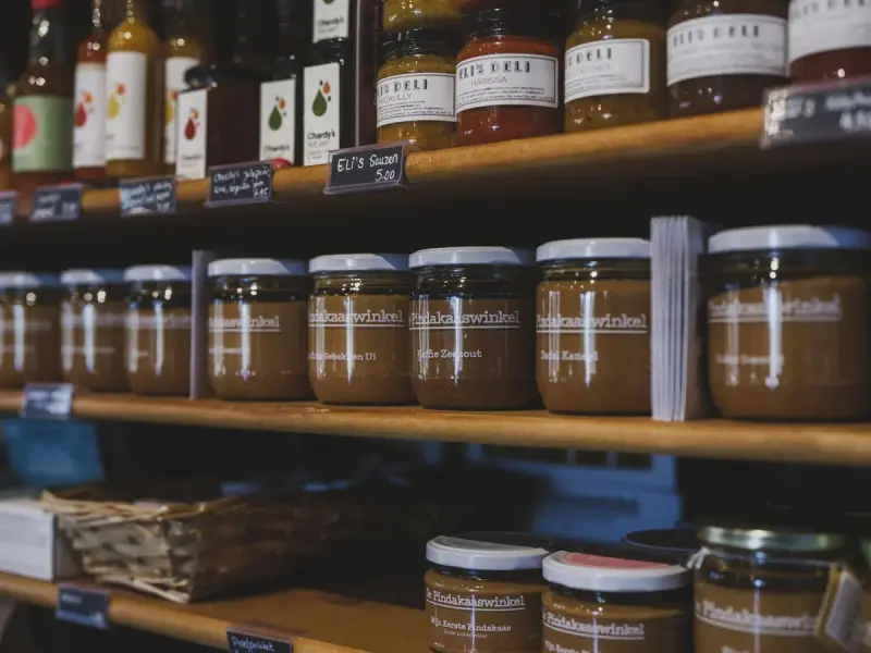 Labeled jars of spreads and sauces on wooden shop shelves with chalkboard price tags