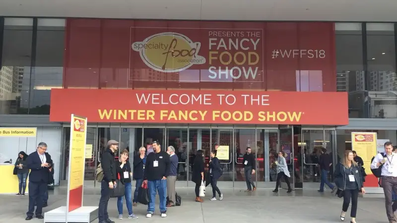 Welcome to the Winter Fancy Food Show banner above the Moscone Center entrance, with the 2018 show hashtag