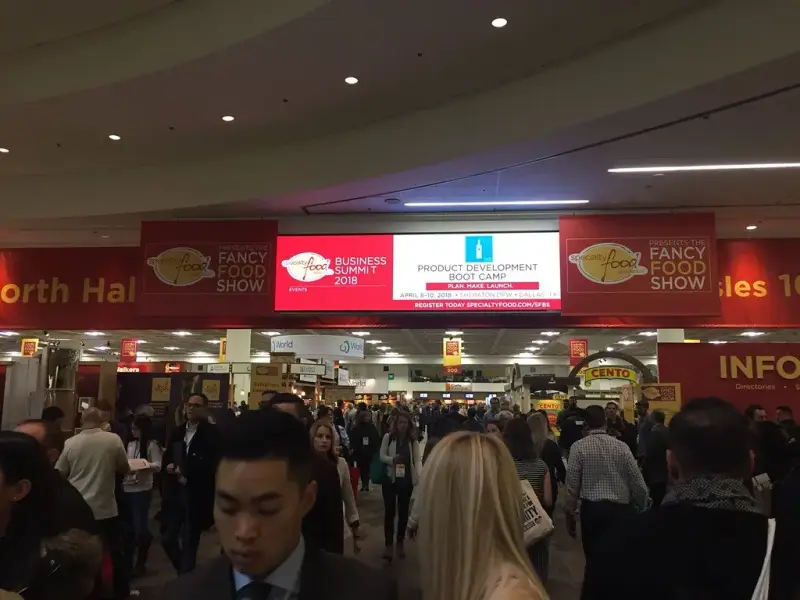 Crowded Winter Fancy Food Show aisle under overhead Fancy Food Show and North Hall banners