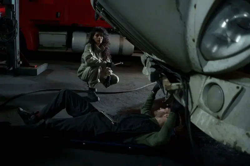 Two mechanics in coveralls working under the front of a truck in a dim service bay