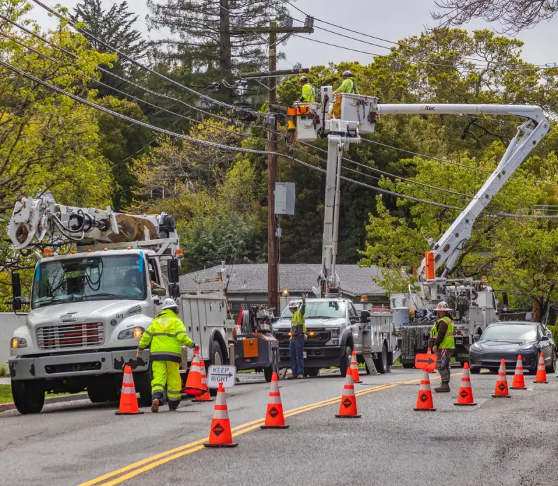 Utility crews in reflective gear working from bucket trucks beside a pole