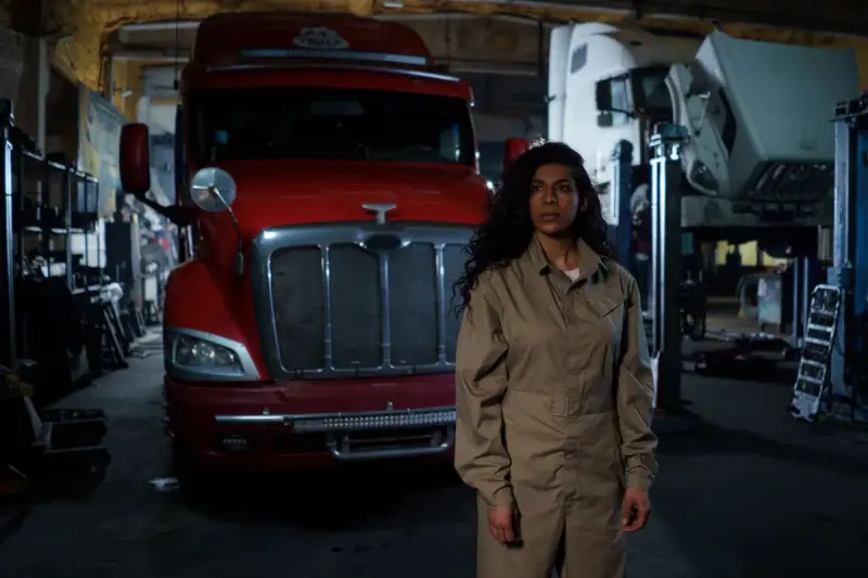 Female mechanic standing in a repair shop with trucks behind her