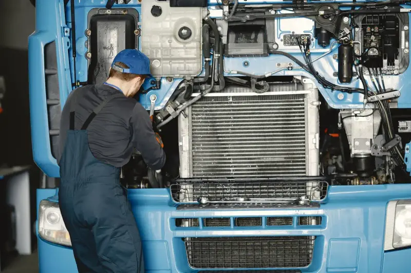 Mechanic in uniform working on the engine of a blue truck
