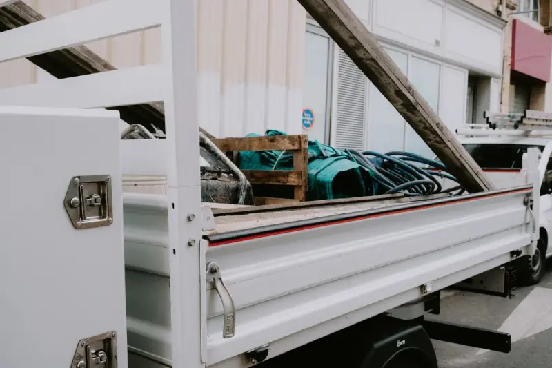 White tipper truck body with a locking toolbox and a load of hoses, crates and lumber