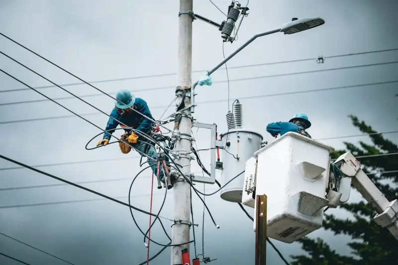 Two line workers in hard hats repairing a transformer pole, one in a bucket truck basket