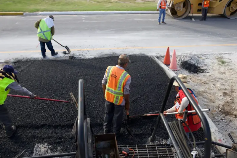 Road workers spreading and leveling fresh asphalt by hand