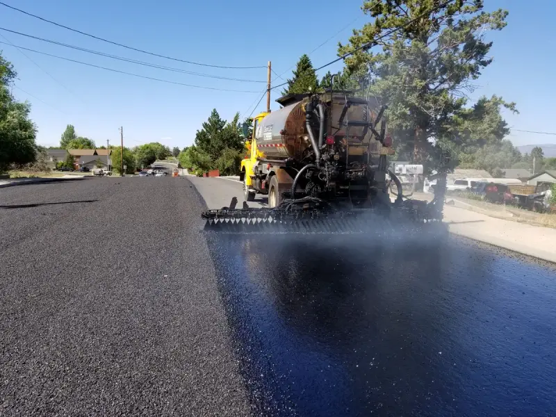 Glossy black tack coat sprayed across a residential street ahead of paving